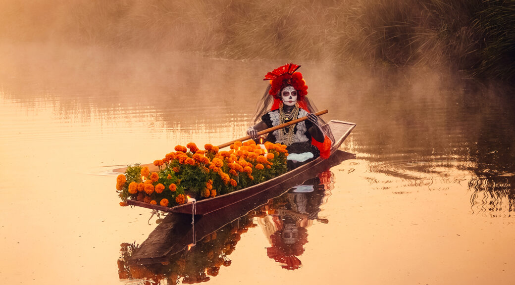 A costumed Día de los Muertos performer ferries marigolds by canoe, a custom linked to guiding ancestral spirits